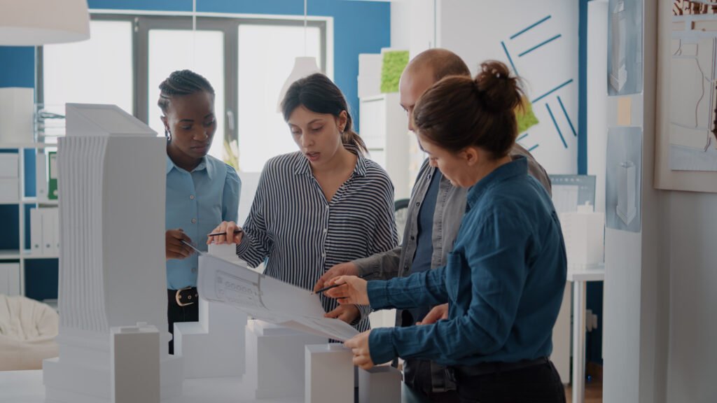 Diverse group of colleagues working on building model design with blueprints plan